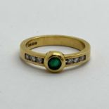 An 18ct Gold Emerald and Diamond Ring, circular collet rubover set to centre, between brilliant