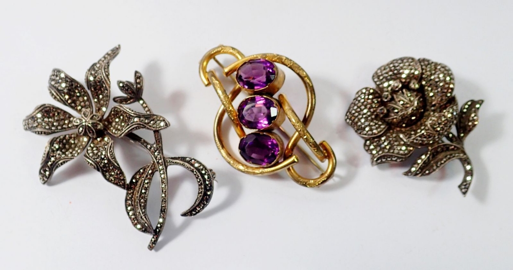 Two silver and marcasite flower form brooches and a Victorian gilt metal and purple glass brooch,