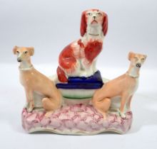 A Victorian Staffordshire group spaniel seated on a cushion flanked by two greyhounds