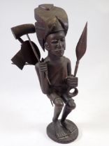 A carved African wood tribal figure holding paddles, club and spear, 36cm tall