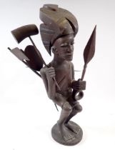 A carved African wood tribal figure holding paddles, club and spear, 36cm tall