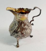 A George III silver cream jug with embossed decoration, gilt interior and three hoof feet, 10cm