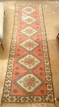 A Turkish style runner with star lozenge decoration on coral ground, 325 x 98cm