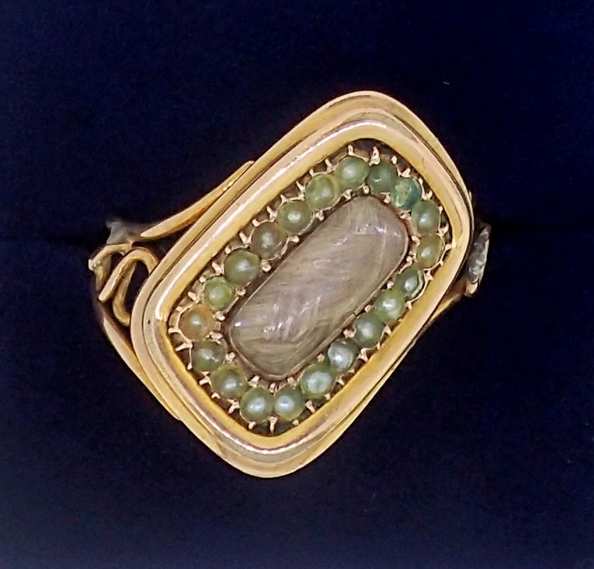 A Victorian gold mourning ring with diagonally set hair locket within seed pearl surround, unmarked,