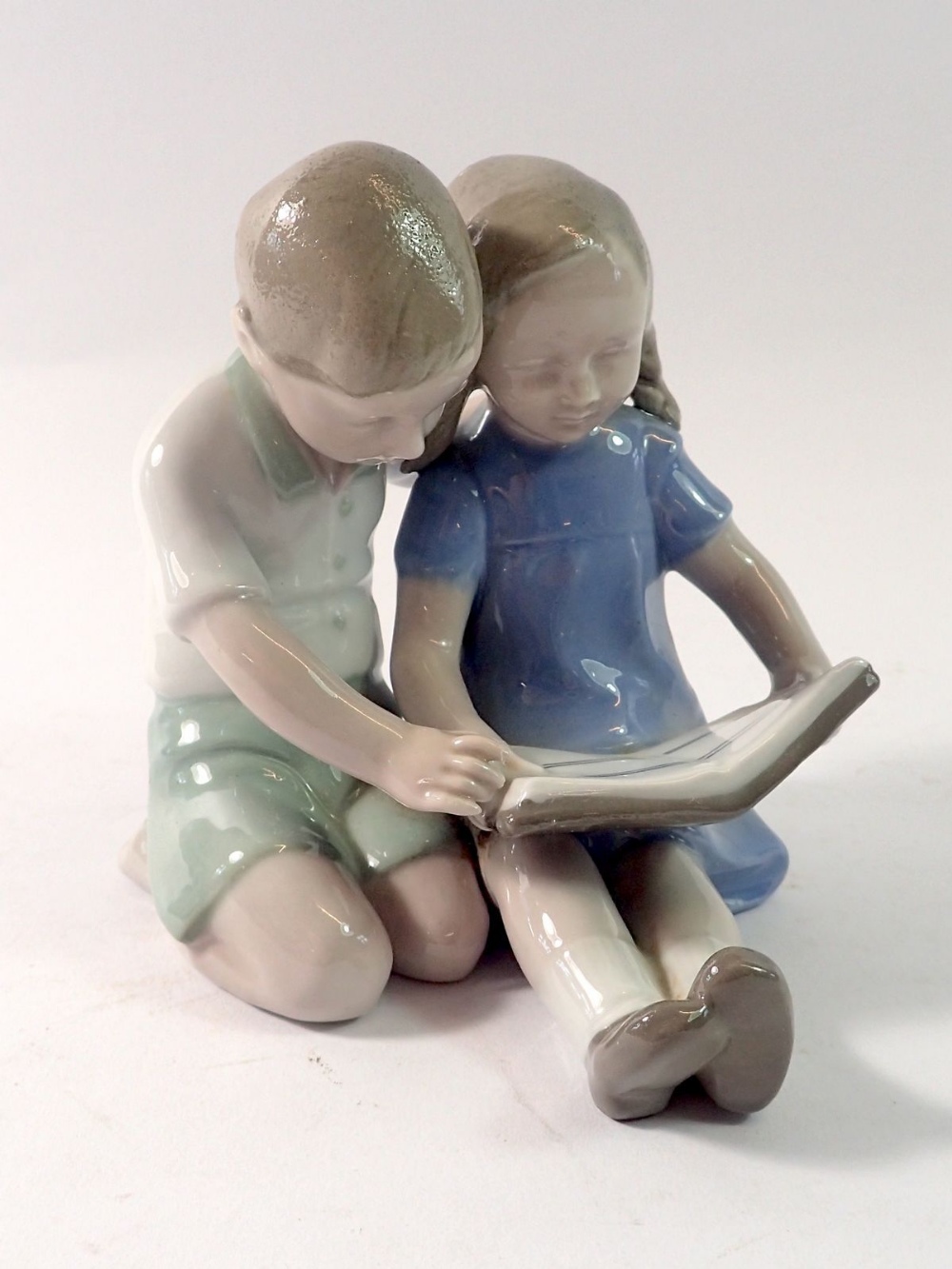 A German porcelain group of two children seated reading by Carl Sheidig, 10cm tall