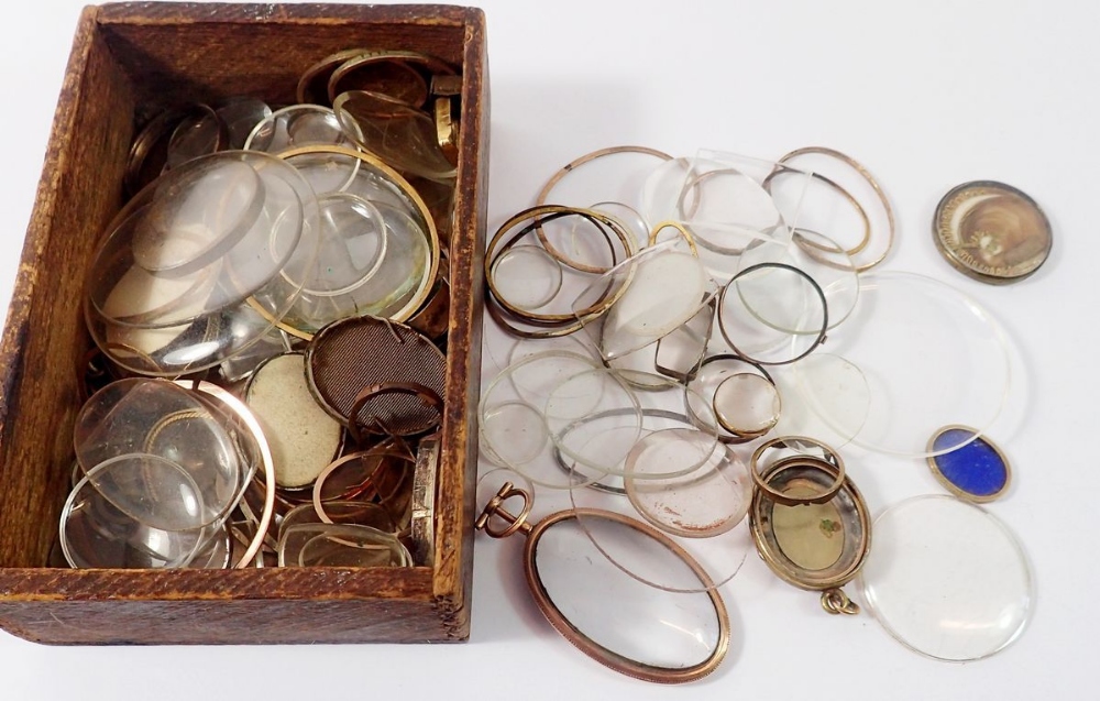 A quantity of antique watch glasses and yellow metal locket surrounds