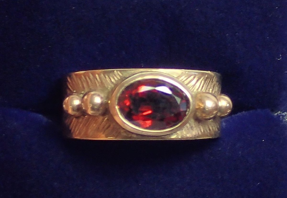 A 9 carat gold ring rub over set oval garnet on wide band and beaded shoulders, size L, 5.3g