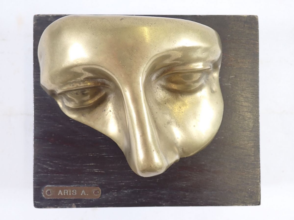 A Venetian brass face mask mounted on a wooden plinth, 'Aris A' 14 x 12cm