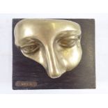 A Venetian brass face mask mounted on a wooden plinth, 'Aris A' 14 x 12cm