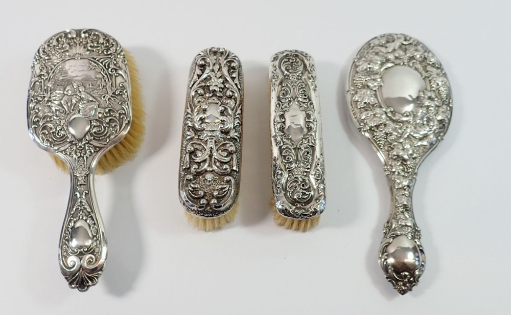 A Victorian silver backed mirror decorated vines and three silver backed brushes