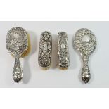 A Victorian silver backed mirror decorated vines and three silver backed brushes