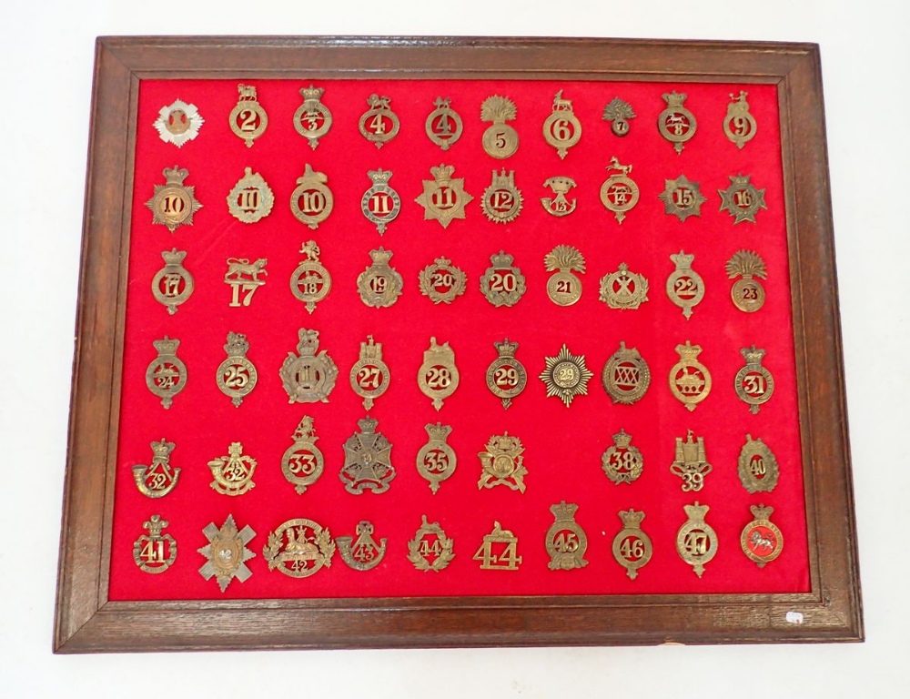 A framed display of fifty nine numbered regimental military cap badges