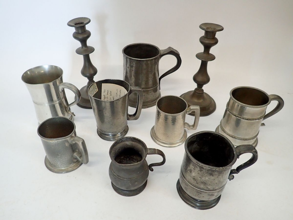 A collection of pewter tankards and a pair of candlesticks