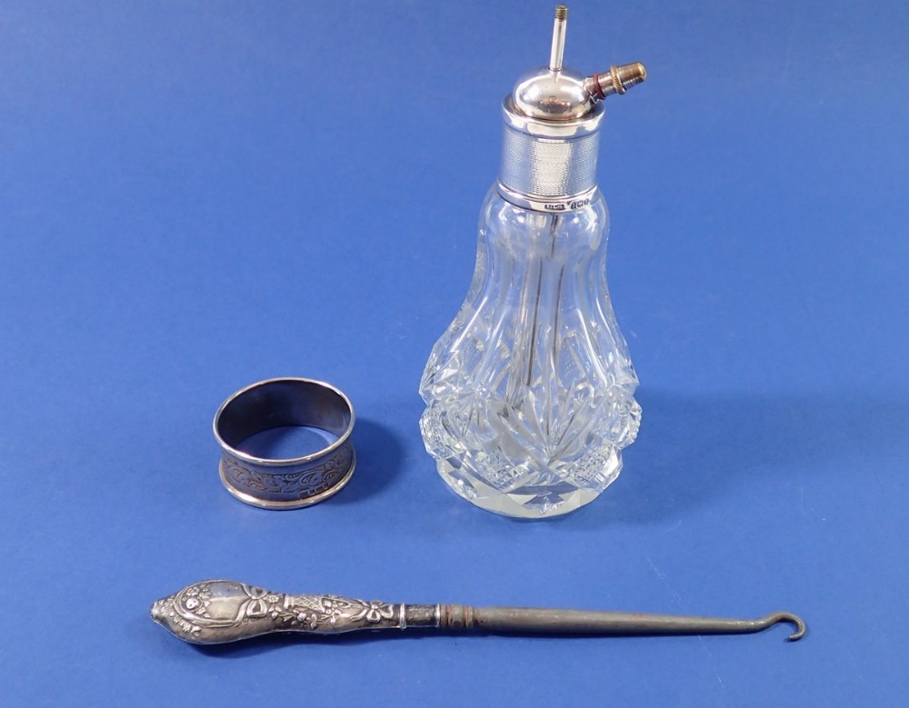 A silver button hook with floral and ribbon decoration, a silver collared cut glass atomiser and a