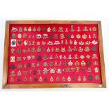 A framed display of one hundred and twenty eight military cap badges