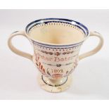 An early 19th century creamware loving cup with glazed annotation 'Peter Bates 1802' and surprise