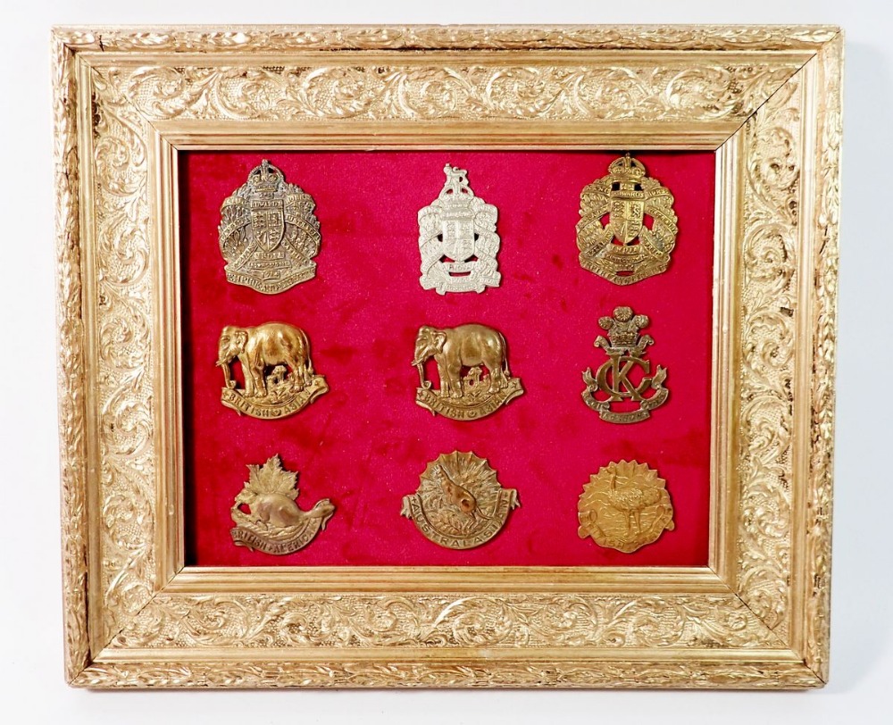 A framed display of British Colonial military cap badges including British Asian, African, American,