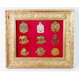 A framed display of British Colonial military cap badges including British Asian, African, American,