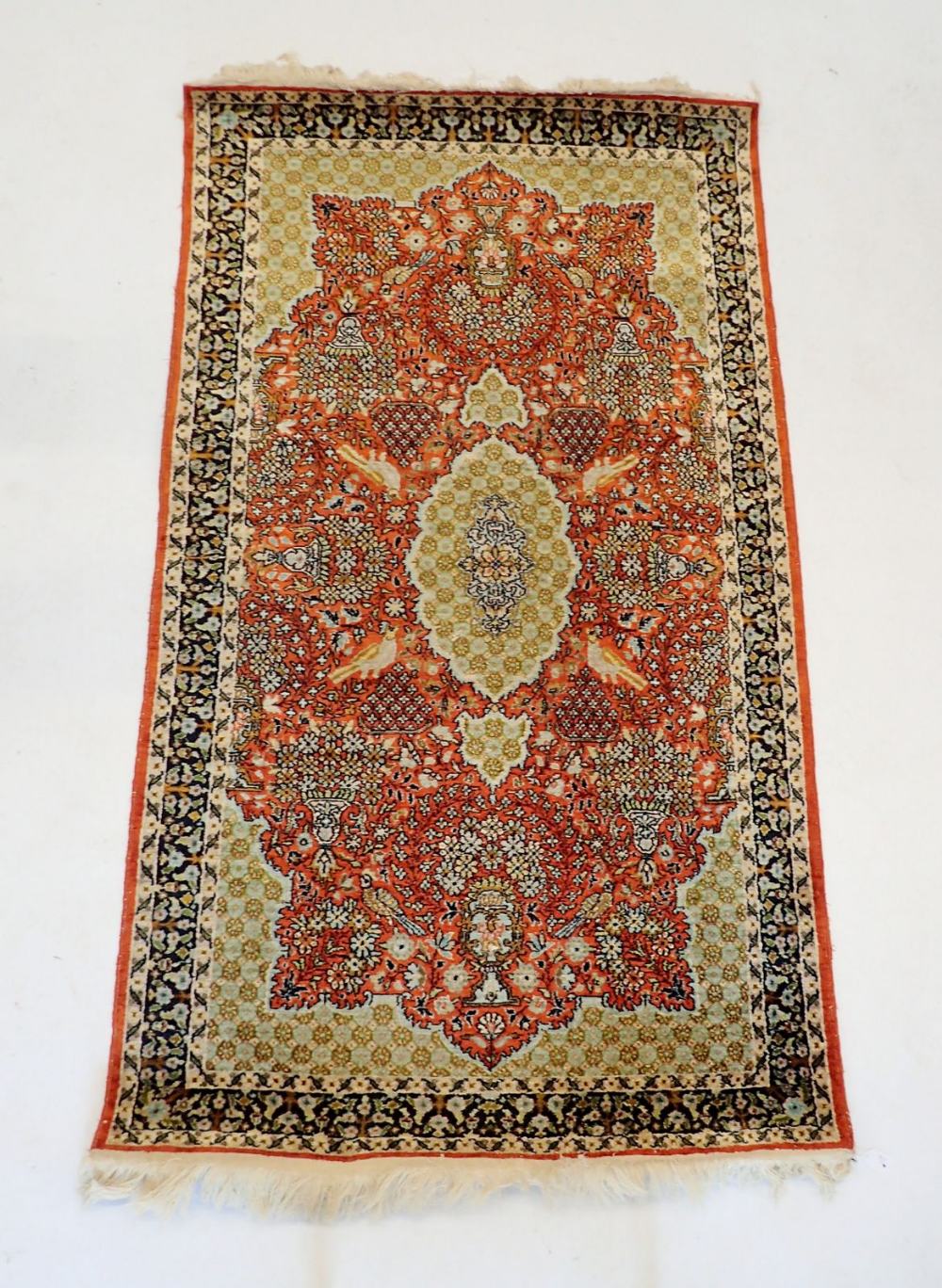 A silk Tabriz rug with bird and stylised floral red medallion on a pale green ground 157 x 91cm