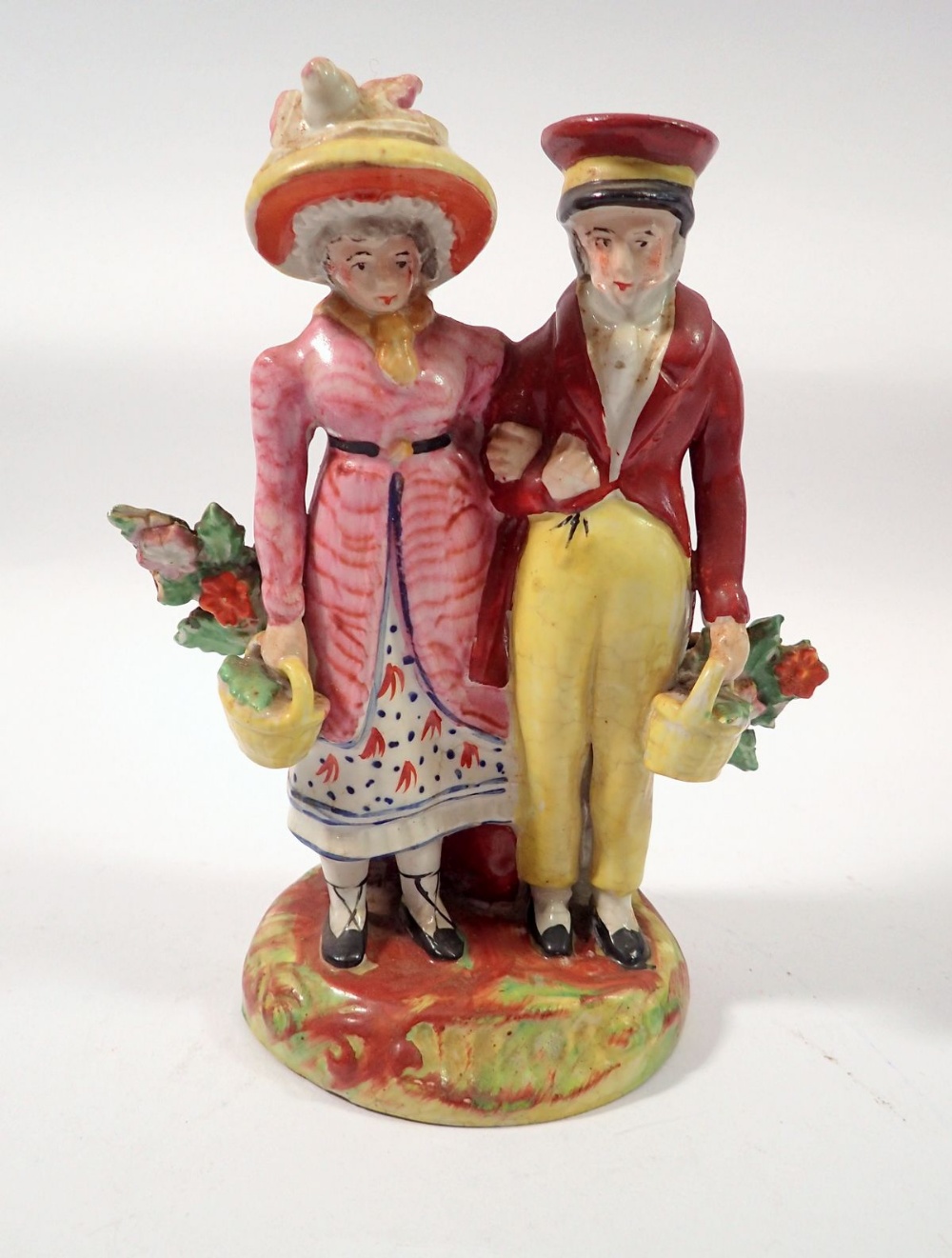 An early Staffordshire group of a man and woman standing with baskets of flowers, 16cm tall