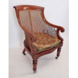 An early Victorian mahogany and cane library chair with scroll over arms on reeded supports