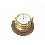 A brass time and tide clock mounted on wood base. Seen running. Postage B