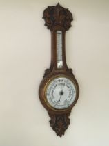 A carved oak wall barometer with a white enamel di