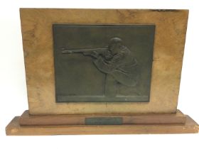 A bronzed olympic shooting plaque mounted on a woo