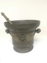 A large bronze Mortar and pestle the sides with raised faces garlands and raised masks.