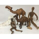 Two leather camel figures a cast and white painted composition stone Roman foot and two wooden dolls