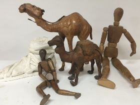 Two leather camel figures a cast and white painted composition stone Roman foot and two wooden dolls