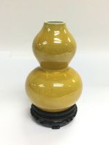 A yellow double gourd vase raised on a hardwood st