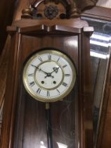 A mahogany wall clock with Arabic Dial and visible pendulum.