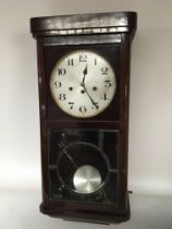 A Mahogany wall clock with a visible pendulum and