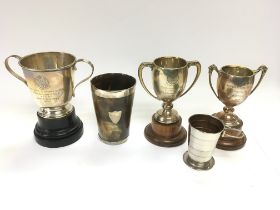 Four silver trophy cups and a collapsing beaker.