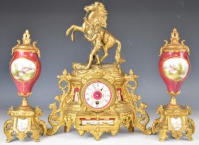 Gilt metal and porcelain mantel clock garniture, the clock surmounted by a man controlling a rearing