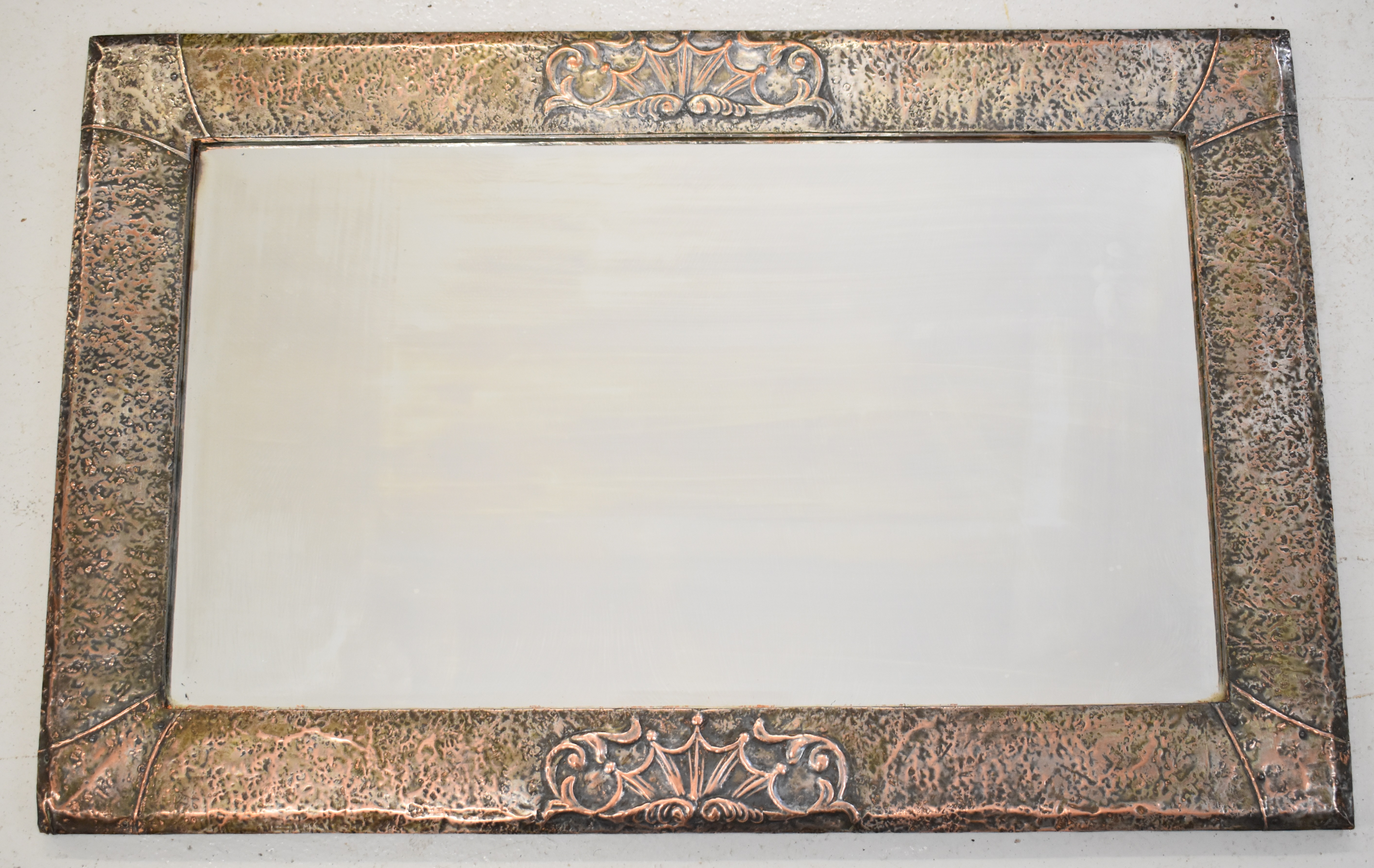 Arts & Crafts copper framed mirror with hammered and relief moulded decoration and bevelled glass