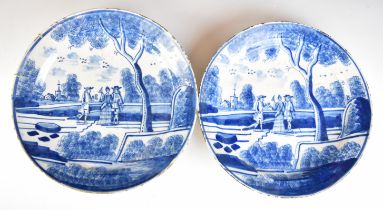A pair of 18th/ 19thC Delft chargers or shallow bowls with decoration of figures in parkland with