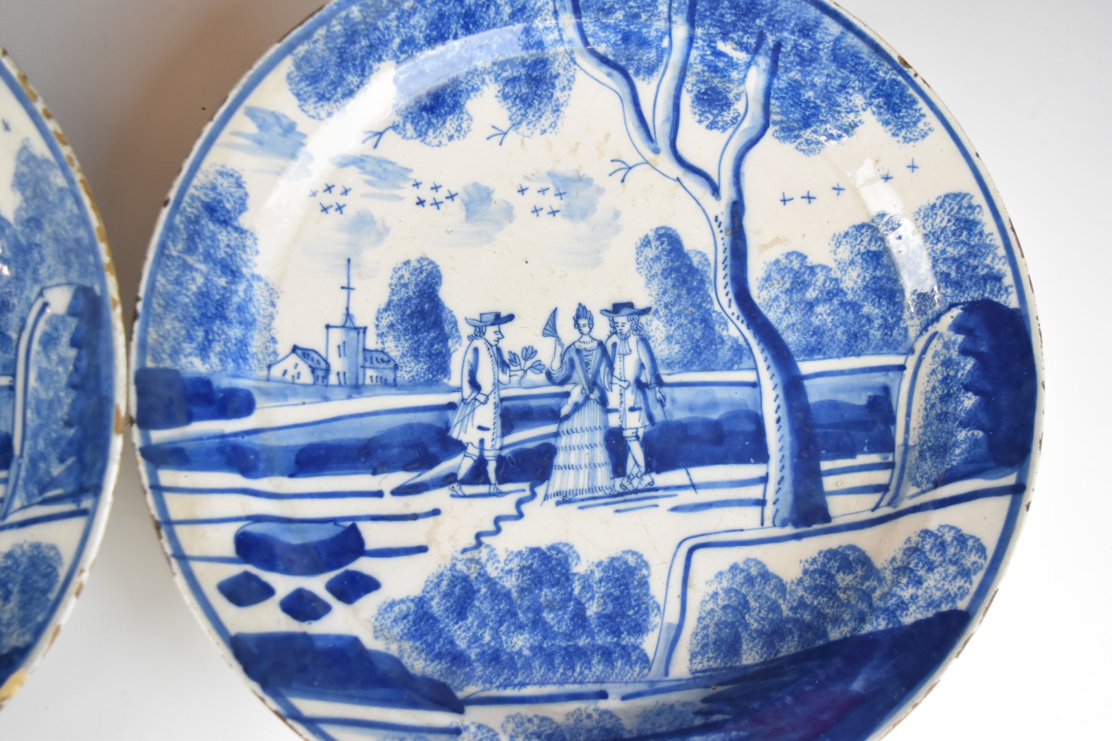 A pair of 18th/ 19thC Delft chargers or shallow bowls with decoration of figures in parkland with - Image 2 of 4