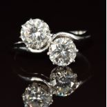 A platinum ring set with two round cut diamonds of approximately 1ct and 1.1ct in a twist setting,