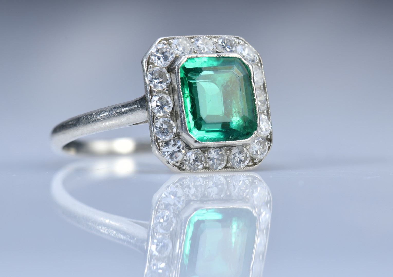 Art Deco platinum ring set with an emerald cut emerald of approximately 1ct surrounded by 16 round