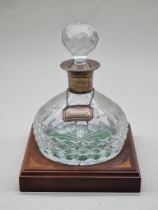 A silver mounted cut glass decanter and stopper, on mahogany and inlaid stand. (2)