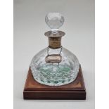 A silver mounted cut glass decanter and stopper, on mahogany and inlaid stand. (2)