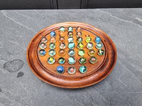 A mahogany solitaire board and thirty six glass marbles, 22cm diameter.
