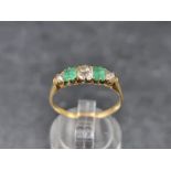 A yellow metal emerald and diamond five stone ring, set three graduated old cut diamonds and two