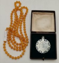 A carved mother-of-pearl disc pendant, and a amber-type bead necklace