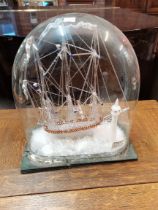 An intricate glass model of a clipper boat in a domed glass with lighthouse and small boat