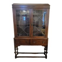 AN EARLY 20TH CENTURY OAK BOOKCASE ON STAND With two glazed doors above drawers and under tier. (