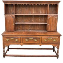 AN 18TH CENTURY OAK DRESSER The cornice above a shaped apron and shelves and two cupboard doors