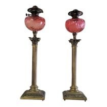 A PAIR OF LARGE EDWARDIAN BRASS OIL LAMPS With cranberry glass bowls above Corinthian capitals and